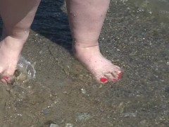 Fat bare legs with red pedicure walk along the bank of the river, fetish.