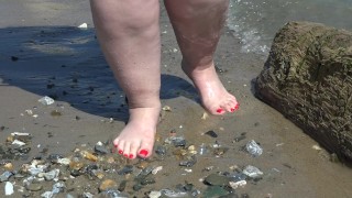 Fat bare legs with red pedicure walk along the bank of the river, fetish.