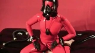 赤いラテックスキャットスーツと防毒マスクを身に着けたスキニーラバーフェチの女の子が自慰行為をする