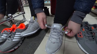 Feticismo del piede in un negozio di scarpe pubblico. Le gambe grasse provano le scarpe da ginnastica.