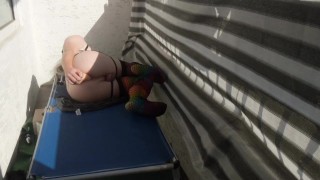 Caged sissy plays with her dildo on public balcony