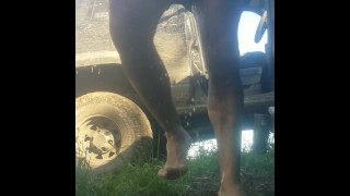 Homem adulto faz xixi em shorts e pés descalços ao ar livre na grama pelo caminhão sujo