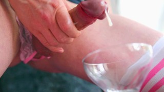 Femboy in open roze slipje streelt zijn rechte grote lul en komt klaar in een glas. Close-up video