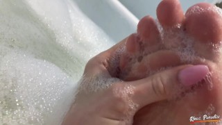 Una bella ragazza fa il bagno e mostra i suoi piedi in una schiuma. Piedi bagnati vicino alla teleca