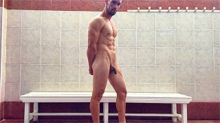 Chico guapo desnudo en vestuario publico mostrando los resultados del entrenamiento del gimnasio