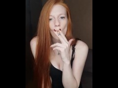 a girl with long red hair smokes a cigarette inhaling deeply smoke