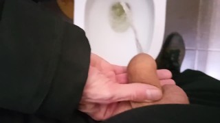 En un lugar público, mi puta femboy sostiene mi polla y me orino en un urinario sucio