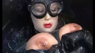 Fille aux gros seins enfermée dans une combinaison en latex en caoutchouc noir profite d’un seau de cumm chaud - partie 2