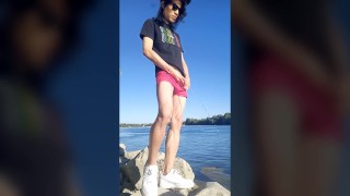 Twink jongen met lang donker haar plassend plassen op de rivier gekleed in een bril met pet sneakers