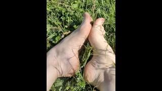 Women's legs pluck grass on a green meadow