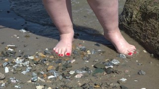 Uma mulher gorda com pés grandes caminha ao longo da costa.