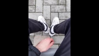 een man in sneakers en witte sokken laat zijn voeten zien in het treinstation