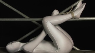Encased girl in shiny zentai suit is tied to a metal pole and tries to escape