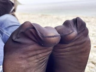 Feet tease in black and grey nylon socks wiggling toes at the seashore