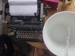 Pissing in the bucket next to typewriter spilling on the table
