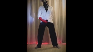 a man in a gas mask, a white shirt, a hat and a red glove plays with his penis
