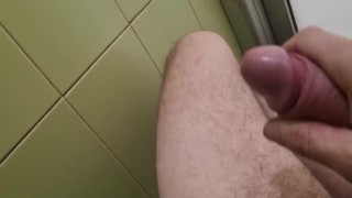 un mec avec une grosse bite se branle dans les toilettes publiques et jouit sur le mur