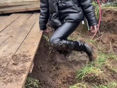 A girl in high-heeled boots likes to get dirty in the mud, she gets her boots dirty up to her knees,